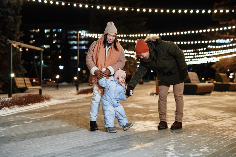 Horizontal shot of stylish Asian couple spending winter evening with their toddler daughter walking together holding hands