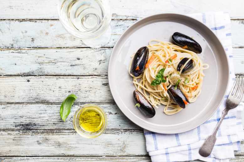 Spaghetti allo scoglio, pasta with seafood, mussels on a gray ceramic plate over wooden background, top view
