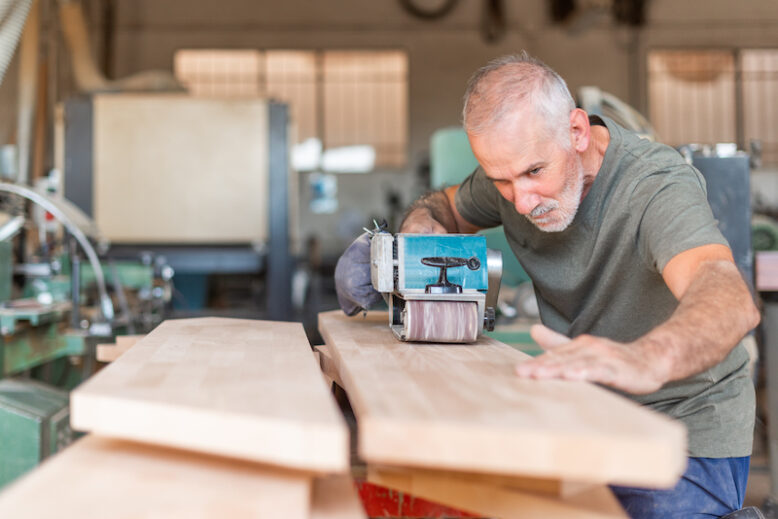 Focused male person working with a hand sander checking the plank