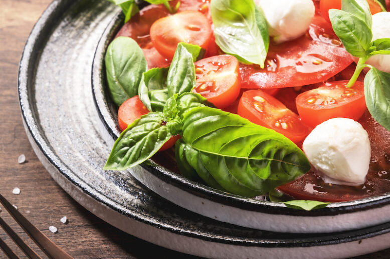 Summer italian salad Caprese with red tomatoes and mozzarella cheese with green basil leaves and olive oil dressing. Top view, wooden table