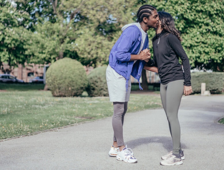 two multiethnic z generation friends greeting cheek to cheek in park before jogging