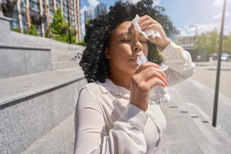 Woman with heatstroke sitting drinking water and drying herself with napkins