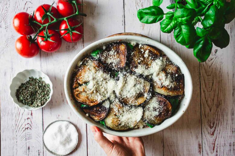 Hand holding casserole dish with assembled Eggplant Parmiagana before baking