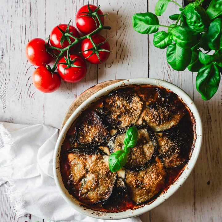 Baked Eggplant Parmiagana with basil on top of white napkin, red tomatoes and green basil