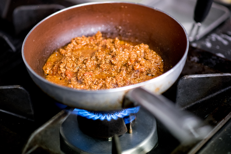Italian savory ragu meat sauce cooking on a gas burner in a restaurant kitchen in preparation for being served on a meal of Italian pasta in a close up view