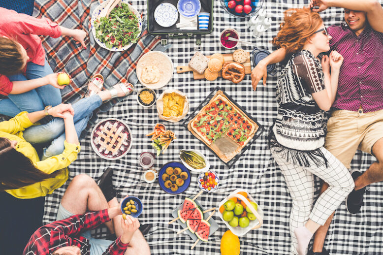 High angle photo of young couple lying on checkered blanket having vegetarian picnic with friends on sunny summer day