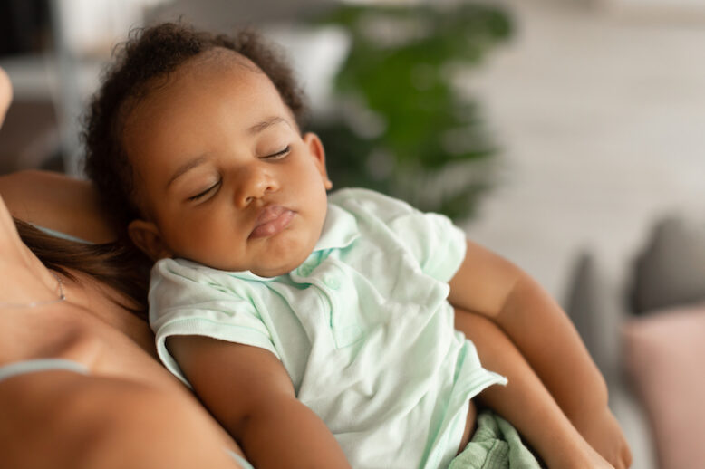 Maternity Concept. Closeup of African American woman holding her adorable small sleeping black baby on hands, singing lullaby, comforting infant kid standing in bedroom at home