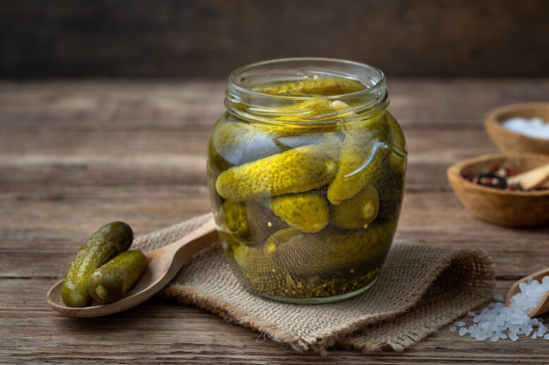 Pickled cucumbers in a glass jar on a wooden table.