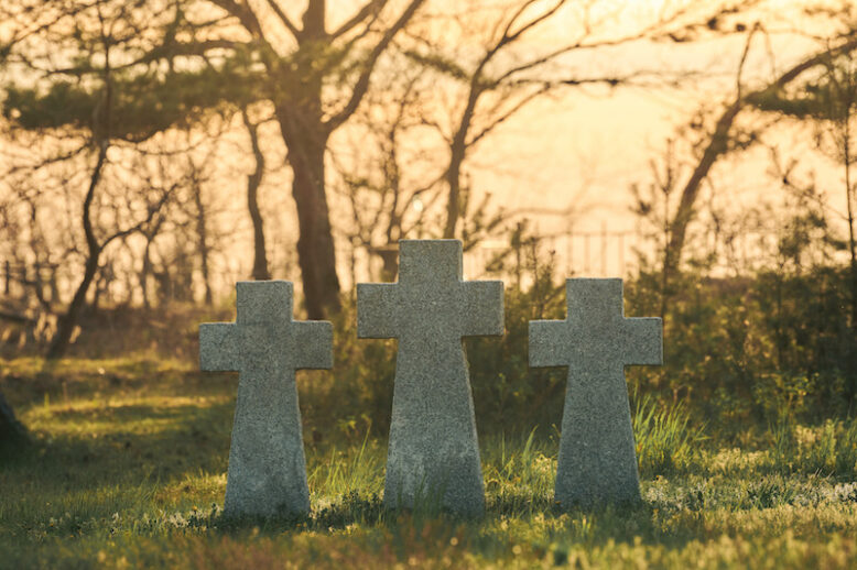 Three catholic stone crosses on green grass at sunset in German military cemetery in Europe. Memorial for dead soldiers of World War II in Baltiysk, Kaliningrad oblast, Russia