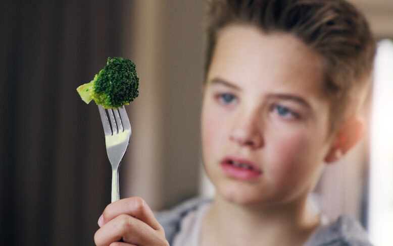 Young boy holding up a fork with a small broccoli.