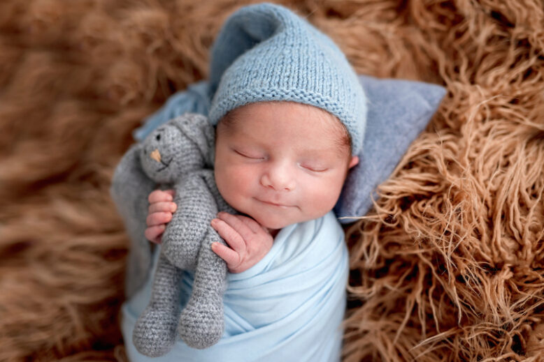 Smiling newborn holding knitted toy in tiny hands while sleeping