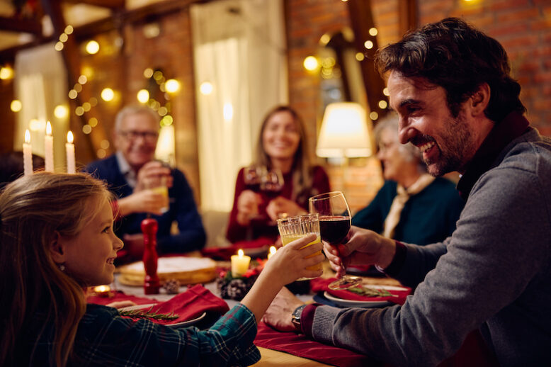 Happy little girl and her father toasting while having dinner with their family on Christmas eve.
