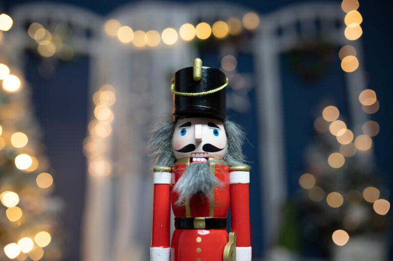 Traditional holiday nutcracker standing in front of decorated Christmas tree