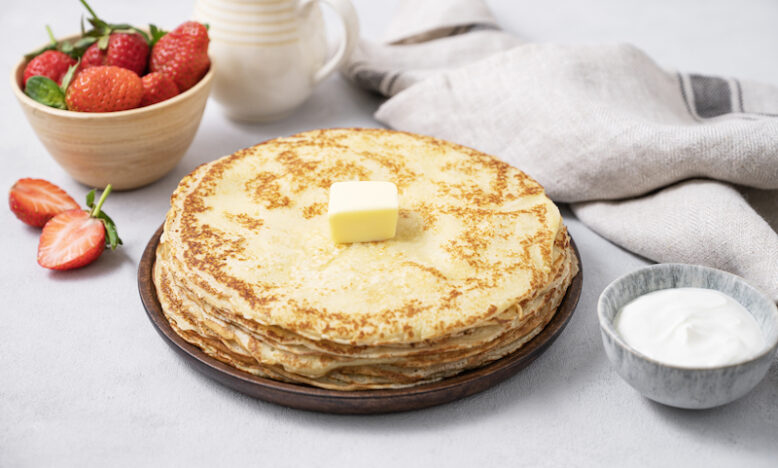 Sweet pancakes stacked with butter, sour cream and fresh strawberries on a light background.