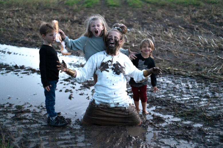 Happy woman playing with three children on muddy field