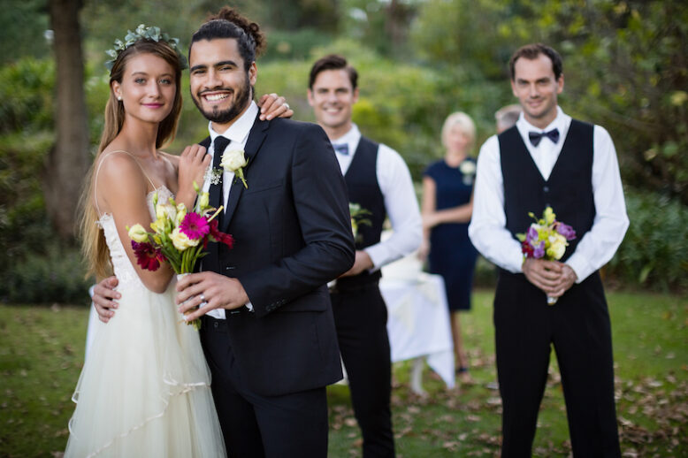 Portrait of wedding couple standing with bouquet of flowers in garden