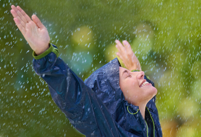 Cropped shot of a young woman dressed in a raincoat enjoying the rain