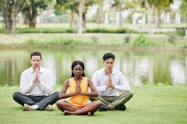 People sitting on meadow in park and practicing yoga and lotus position