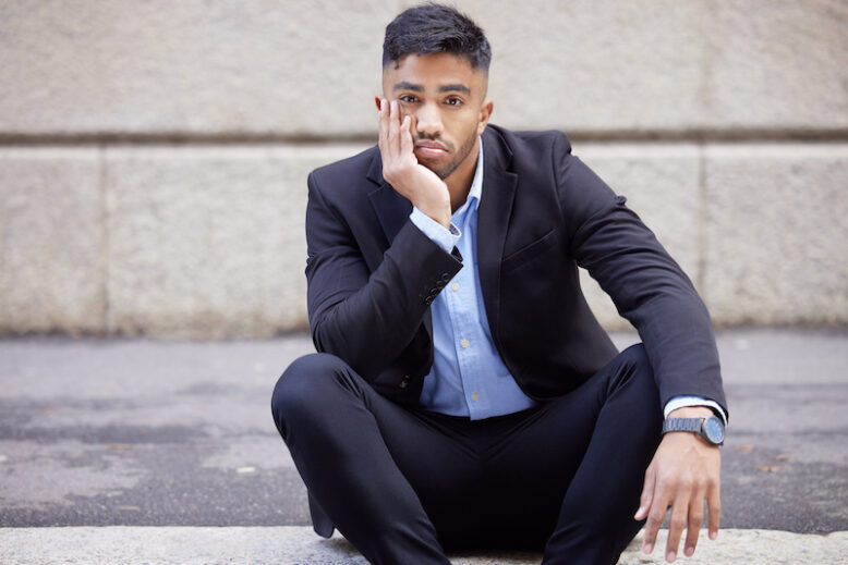 Shot of a handsome young businessman sitting and looking bored in the city.
