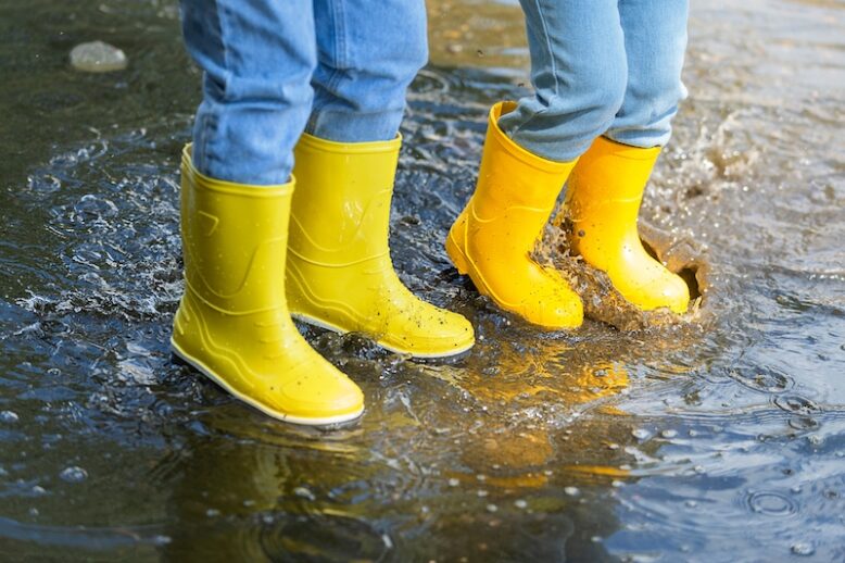 Close-up on kids jumping in a paddle with yellow boots.