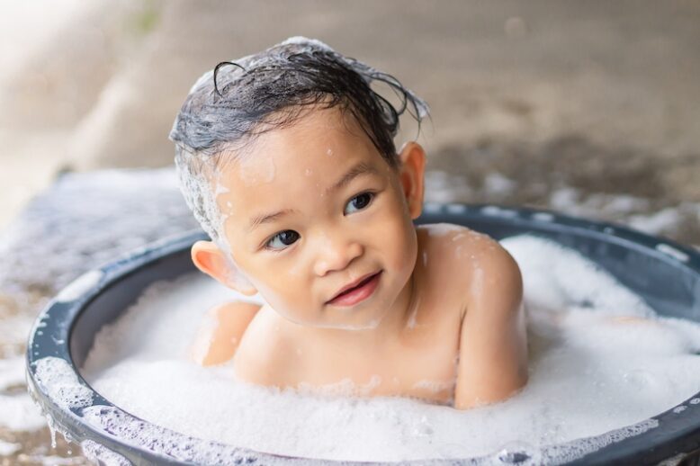 Portrait image of 1-2​ years old baby. Happy baby Asian girl take a bath with bubbles soap and playing a ball toy. She sitting in a bathtub. Sweet smiling.