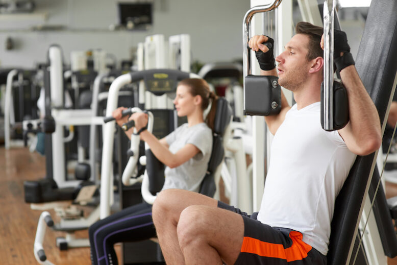 Young man and woman doing exercise on chest press. 