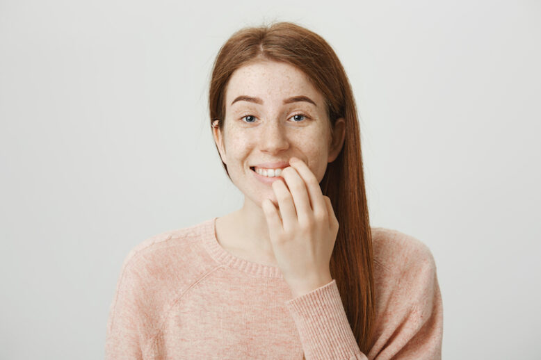 Funny emotive girl with bad habit, biting nails on fingers while looking at camera