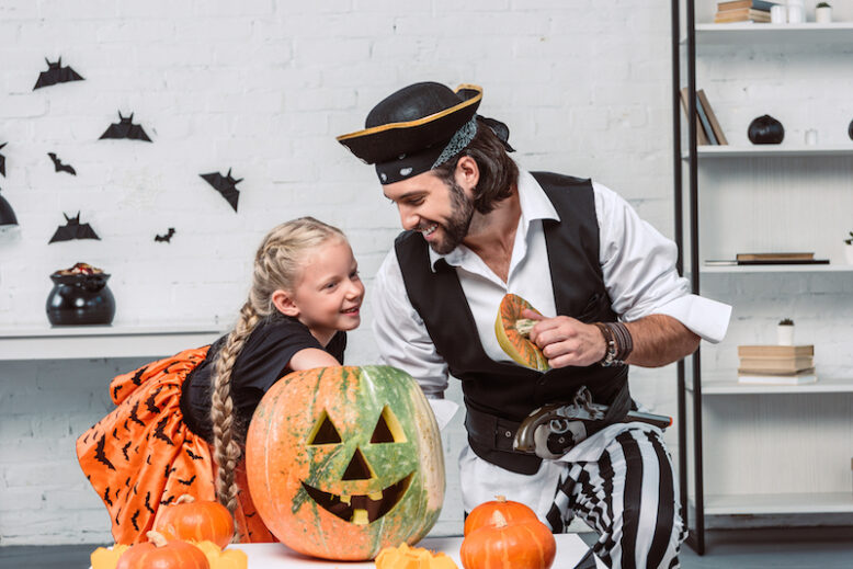 father and daughter in halloween costumes looking into pumpkin together at home