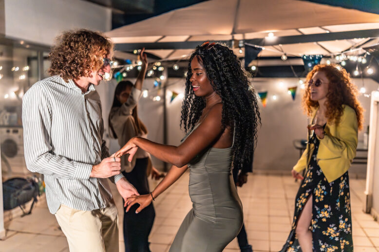 Multi-ethnic friends dancing holding hands latin music at night party in a terrace