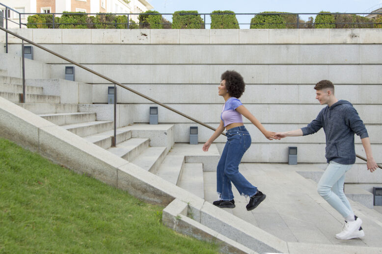 Young caucasian man behind afro woman climbing stairs