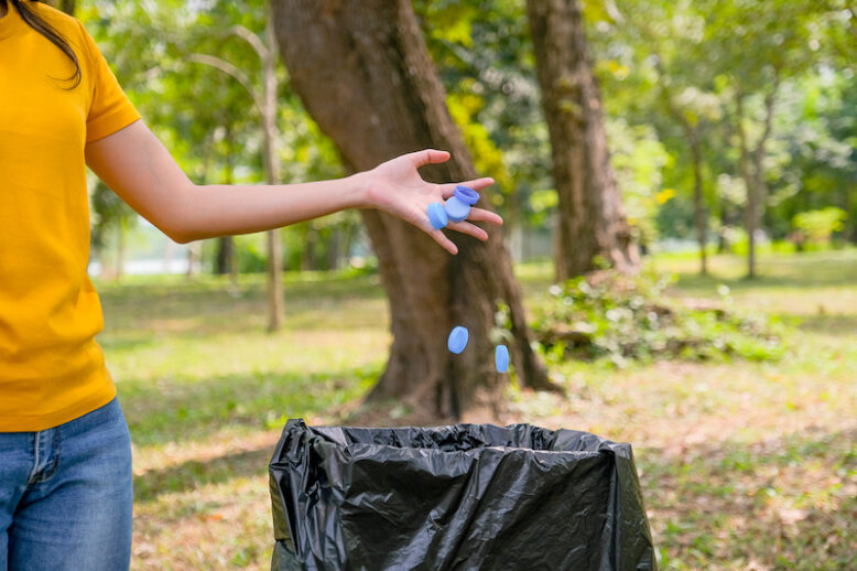 Hand of yellow t-shirt woman hold lot of bottle caps in the park or garden.