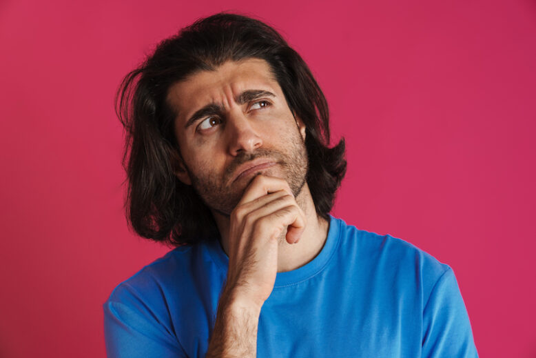 Puzzled brunette man in t-shirt think and looking upward isolated over pink background