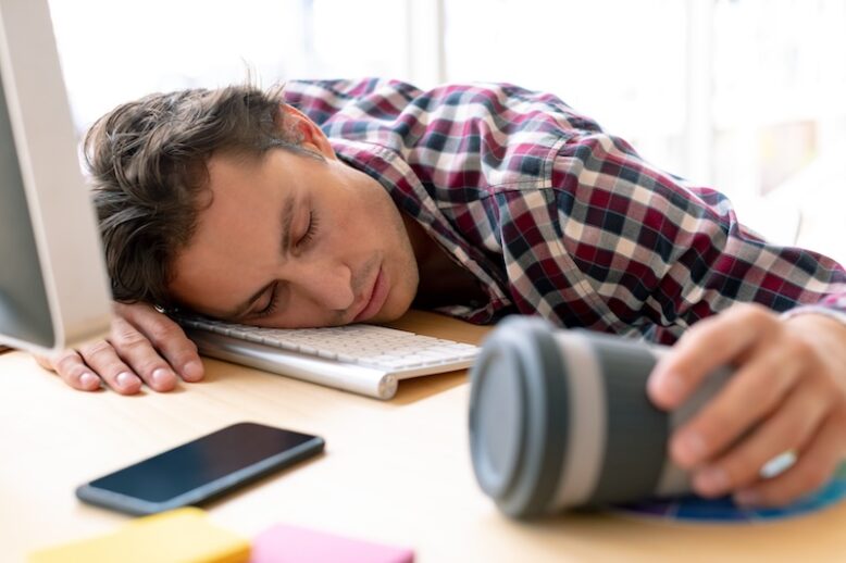 Tired male graphic designer sleeping on desk in a modern office