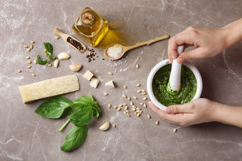 Woman mixing pesto sauce with pestle in mortar on grey table