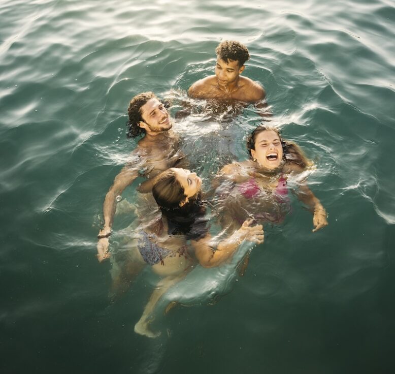 Group of cheerful young friends having fun, bathing together in the sea during summer holidays