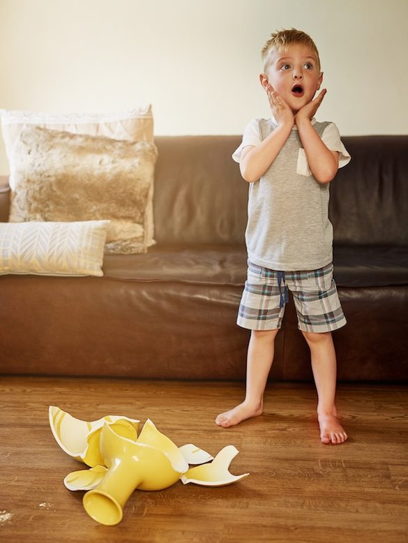 Little boy looking shocked after breaking a vase at home.