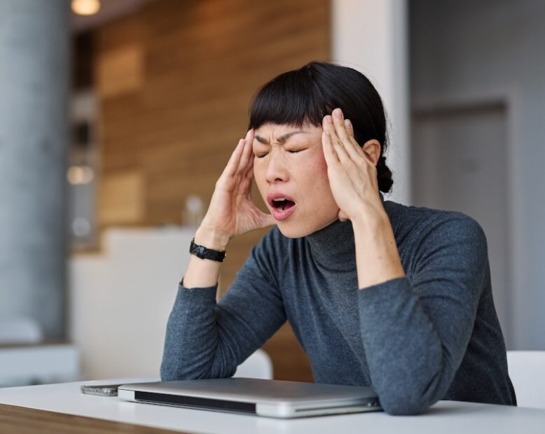 Business woman sitting at a table, feeling tired and touching her head.